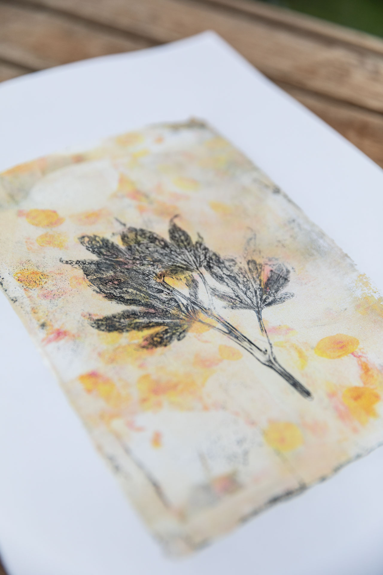 Gel Print mit einem schwarzen Herbstblatt auf Gelb- und Goldtönen auf DIN A 4.
